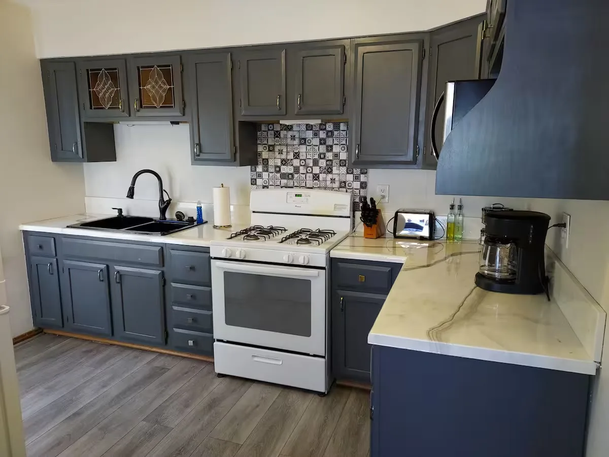 Kitchen with gray cabinets, white gas range, coffee maker and stone-look counters at The Family Comfort in St. Louis