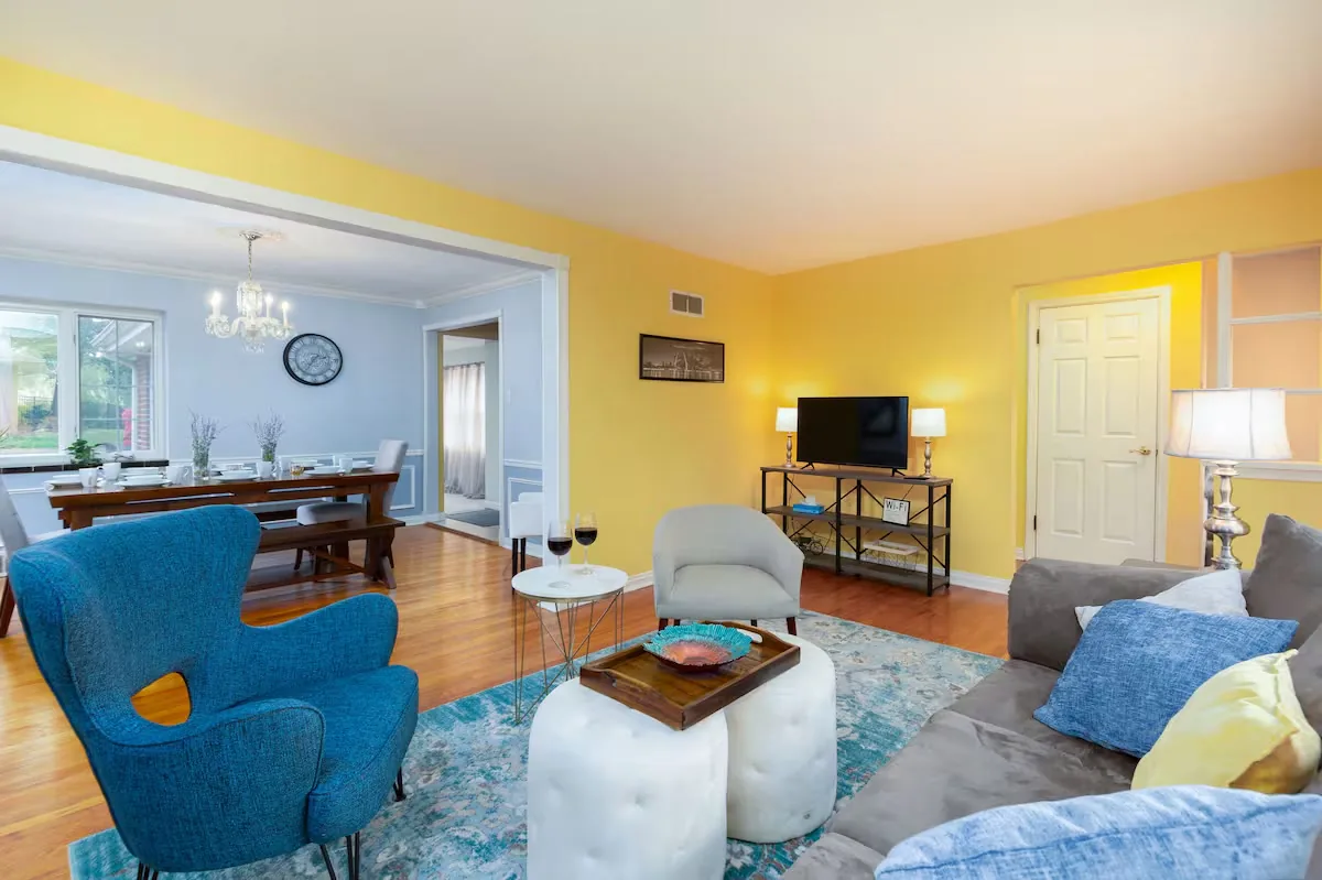 Bright living room with a gray sofa, blue armchair and dining room beyond at The Heritage House, a furnished Arch City Stays home in St. Louis